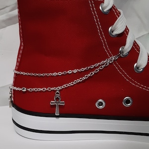 May include: Red high-top canvas sneakers with white laces and a silver chain anklet with an ankh charm.