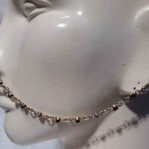 Pode incluir: Uma corrente de nariz dourada com um design de corrente delicado. A corrente é adornada com pequenas pedras preciosas coloridas, incluindo pedras claras, castanhas e pretas. A joia foi projetada para ser usada com um piercing no nariz e uma perfuração na orelha.