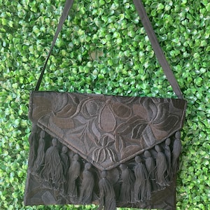 May include: Black embroidered clutch bag with a flap closure and tassel trim.