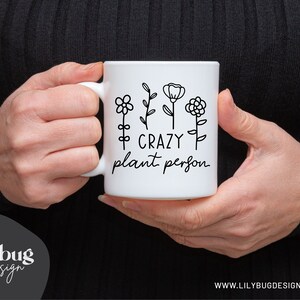 May include: White ceramic mug with a black outline of flowers and the text "Crazy plant person".
