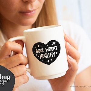 K&ouml;nnte beinhalten: Wei&szlig;e Keramiktasse mit einem schwarzen Herzdesign, auf dem "Goal Weight Healthy" mit wei&szlig;en Sternen um das Herz steht.