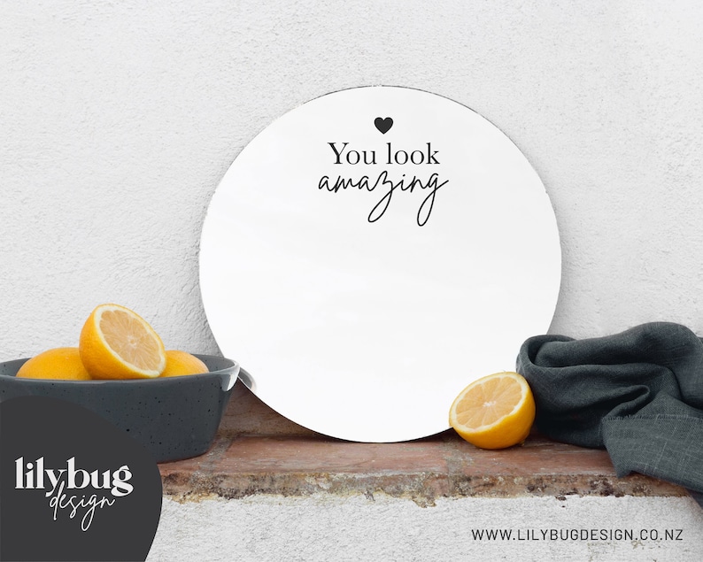 K&ouml;nnte beinhalten: Runder wei&szlig;er Spiegel mit dem Text "You look amazing" in schwarzer Schrift mit einem kleinen schwarzen Herzen &uuml;ber dem Text.