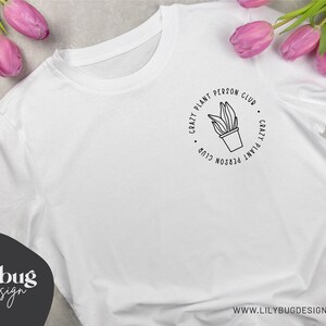 May include: White t-shirt with a black graphic design that says "Crazy Plant Person Club" with a plant in a pot in the center.