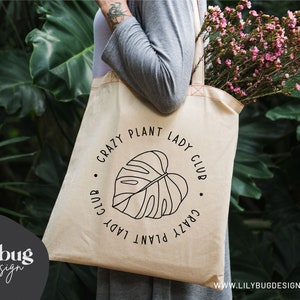May include: A beige tote bag with a black graphic of a monstera leaf and the text "Crazy Plant Lady Club".