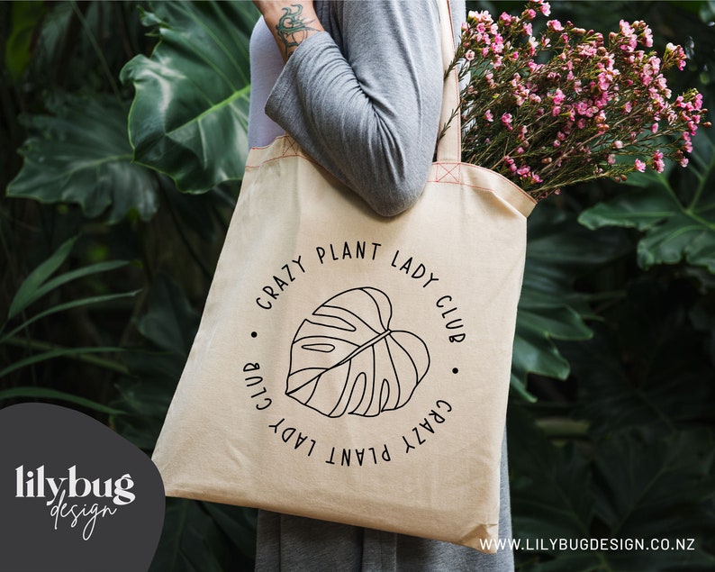 May include: A beige tote bag with a black graphic of a monstera leaf and the text "Crazy Plant Lady Club".