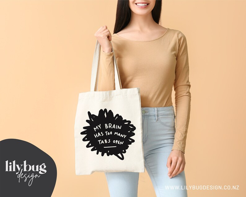 May include: A white tote bag with black text that reads "My brain has too many tabs open". The text is in a hand-drawn style and is surrounded by a black scribble.