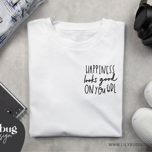 May include: White t-shirt with black text that reads "Happiness looks good on you girl".