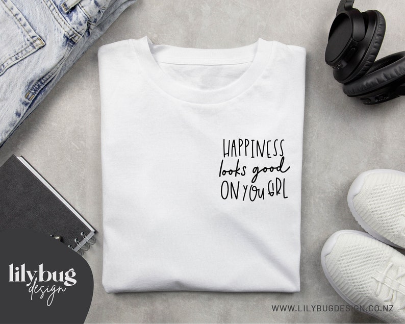 May include: White t-shirt with black text that reads "Happiness looks good on you girl".