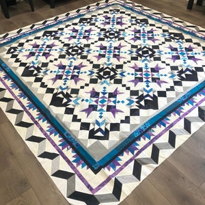 May include: A large quilt with a geometric pattern in shades of blue, purple, white, and black. The quilt is made up of squares and triangles, and the pattern is repeated throughout the quilt.