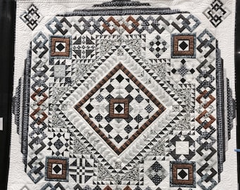 May include: A square quilt featuring a complex geometric pattern in black, white, gray, and copper tones. The design includes a central diamond, intricate border motifs, and four corner squares, all finished with detailed white machine quilting stitches.