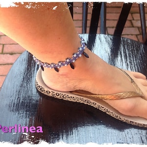 Può includere: Primo piano di una caviglia di donna che indossa un braccialetto per caviglia con perline con accenti neri e viola. Il braccialetto è fatto di piccole perline e ha un design delicato. Il braccialetto è indossato su una caviglia nuda e la donna indossa un paio di infradito con un design a stampa leopardata.