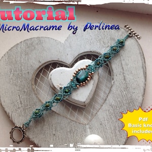 May include: A teal micro-macrame bracelet with a central oval stone and copper-coloured beads. The bracelet is displayed on a white heart-shaped wooden background. Text includes "Tutorial MicroMacrame by Perlinea" and "Pdf Basic knots included".