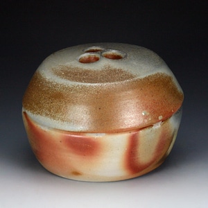 May include: A round ceramic vessel with a lid featuring three circular openings on top. The piece has a mottled glaze finish in shades of cream, tan, and reddish-brown, with a smooth, rounded silhouette and a horizontal seam where the lid meets the base.