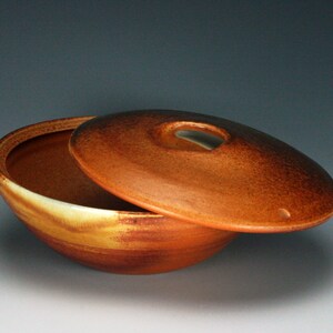 May include: A ceramic bowl with a lid, both glazed in a brown and yellow color. The lid has a small hole in the center.