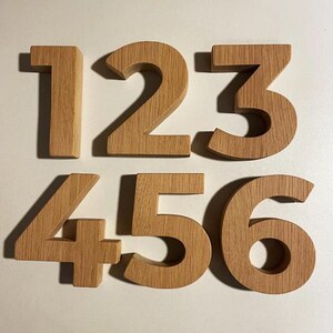 Peut inclure: Chiffres en bois 1, 2, 3, 4, 5 et 6. Chaque chiffre est fabriqué en bois clair, mettant en valeur le grain naturel. Les chiffres sont disposés sur deux rangées, chacun projetant une ombre.