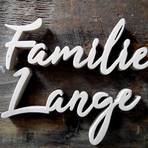 Könnte beinhalten: Ein weißes Holzschild mit den Worten "Familie Lange" in einer kursivschrift.