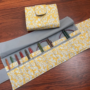 May include: A yellow and white floral print knitting needle case and matching wallet. The case is open, revealing several knitting needles in various colours. The case is grey on the inside and has a snap closure. The wallet has a flap closure.