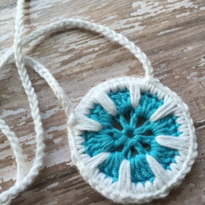 May include: A white crocheted necklace with a blue and white crocheted flower pendant.