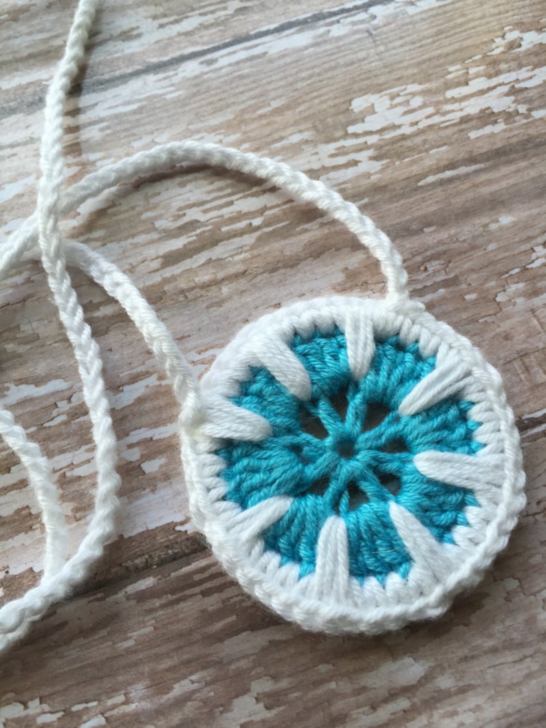May include: A white crocheted necklace with a blue and white crocheted flower pendant.