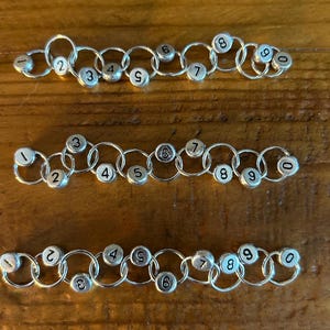 May include: A set of ten silver-toned metal rings with numbers 1 through 10 printed on them. The rings are linked together in a chain.