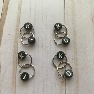 May include: Four sets of black and silver stitch markers with the letter K and the letter I or O on them.