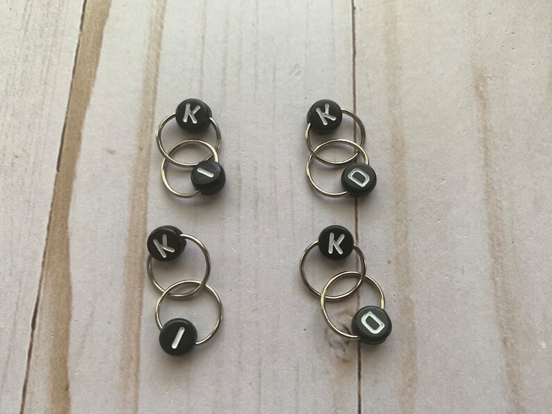 May include: Four sets of black and silver stitch markers with the letter K and the letter I or O on them.