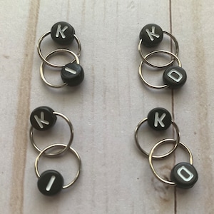 May include: Four sets of black and silver knitting stitch markers with the letter K and the number 0 on them.