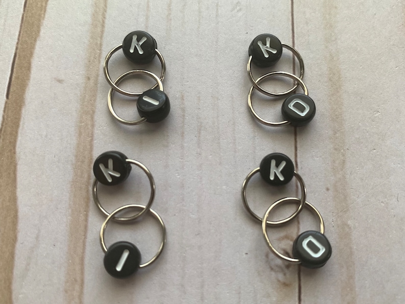 May include: Four sets of black and silver knitting stitch markers with the letter K and the number 0 on them.