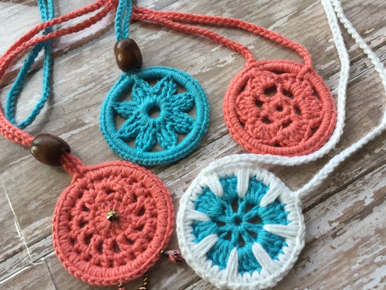 May include: Four crocheted necklaces with round, colorful, floral-patterned pendants. The necklaces are made with a variety of colors, including blue, white, and coral.