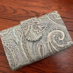 May include: A gray and teal paisley patterned fabric wallet with a flap closure.