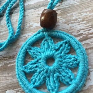 May include: A turquoise crocheted necklace with a wooden bead. The necklace features a circular pendant with a six-pointed star design.