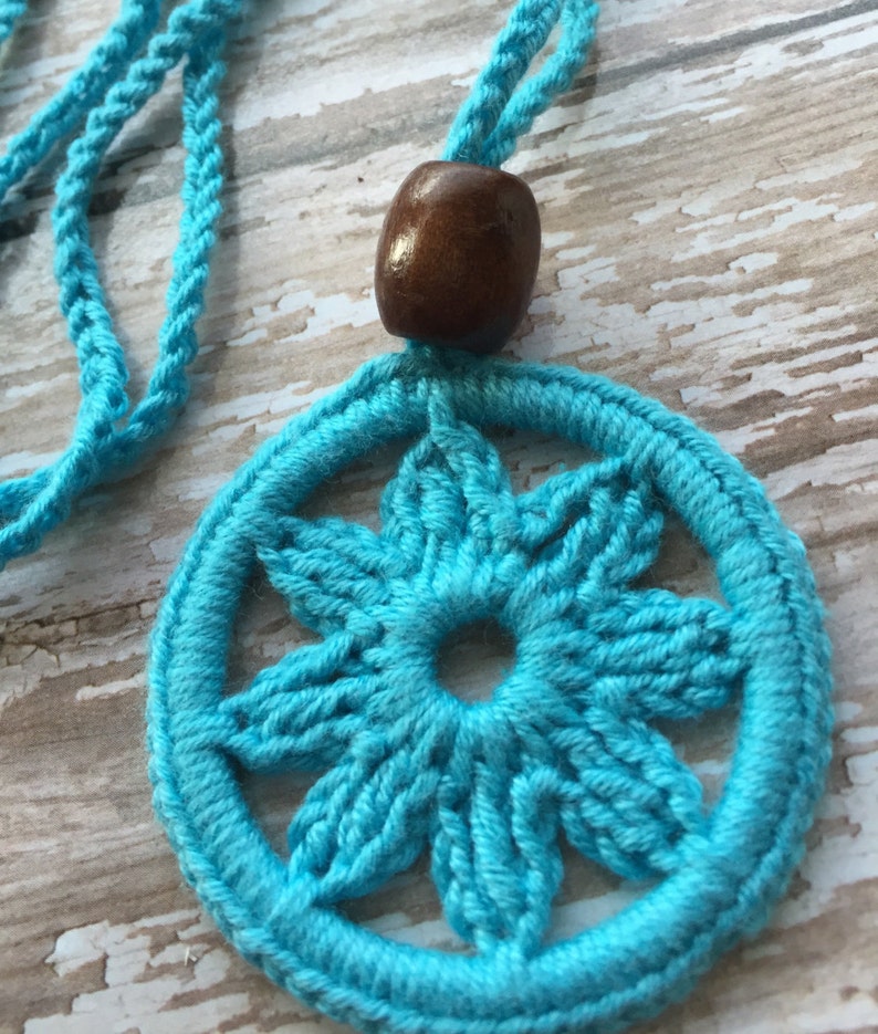 May include: A turquoise crocheted necklace with a wooden bead. The necklace features a circular pendant with a six-pointed star design.