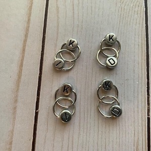 May include: Four sets of silver metal ring stitch markers with the letter K on one ring and the letter I on the other ring.