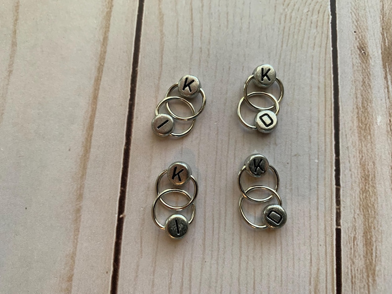 May include: Four sets of silver metal ring stitch markers with the letter K on one ring and the letter I on the other ring.