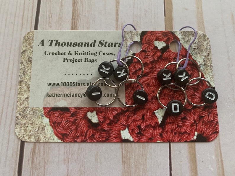 May include: A set of six black and white stitch markers with letters K, I, and D. The markers are on a card that says "A Thousand Stars Crochet & Knitting Cases, Project Bags".