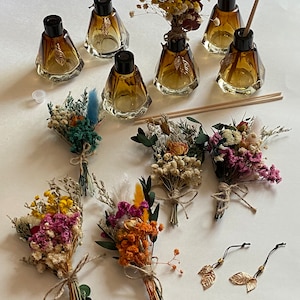 May include: Set of six amber glass diffuser bottles with black lids and gold leaf accents. Each bottle is paired with a small bouquet of dried flowers in various colors, including pink, yellow, orange, and green. Two gold leaf charms are also included.