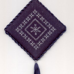 May include: A dark blue fabric ornament with a silver snowflake design and a tassel. The ornament has a loop at the top for hanging.