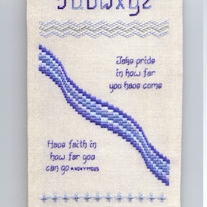 May include: A white fabric scroll with a blue and purple embroidered alphabet, a blue and purple embroidered wave design, and the text "Take pride in how far you have come" and "Have faith in how far you can go ANONYMOUS".