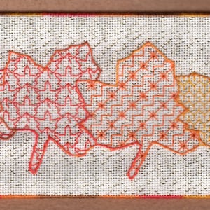 May include: A white fabric with four embroidered maple leaves in shades of red, orange, and yellow. The leaves are arranged in a row and have intricate geometric patterns.