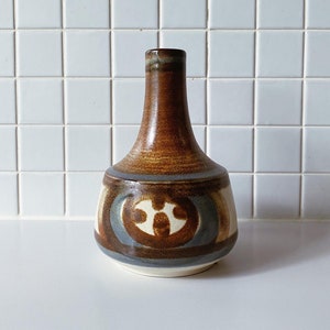 Könnte beinhalten: Eine braune Keramikvase mit einem geometrischen Muster in Blautönen, Weiß und Braun. Die Vase hat einen schmalen Hals und einen breiten, abgerundeten Boden.