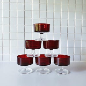 Könnte beinhalten: Satz mit sechs klaren Dessertgläsern mit burgunderroter Basis. Die Gläser sind pyramidenförmig gestapelt.