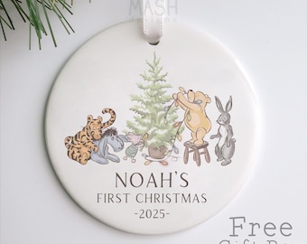 Könnte beinhalten: Weißer Keramik-Weihnachtsschmuck mit Winnie-the-Pooh-Figuren, die einen Weihnachtsbaum schmücken. Der Schmuck enthält den Text "NOAH'S FIRST CHRISTMAS -2025". Ein weißes Band ist zum Aufhängen befestigt.