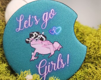 May include: Teal blue round coaster with a pink frog wearing a cowboy hat and the text "Let's go girls!" in pink lettering.