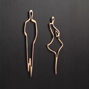 May include: Gold metal outline of a person in a dress and a person in pants, on a black background.