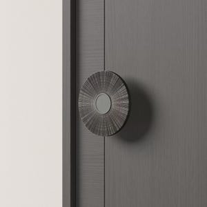 May include: A dark gray, circular door handle with a textured, radial design. The handle has a central, circular, silver-colored accent. The handle is mounted on a gray door with vertical wood grain.