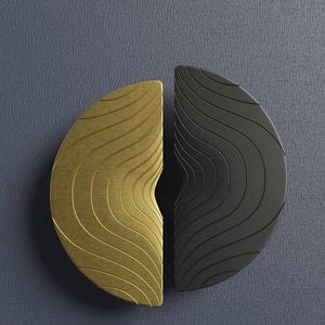 May include: Two half-circle cabinet pulls. One is gold-toned with a wavy, textured surface, and the other is black with a similar design. The pulls are set against a textured, dark blue background.