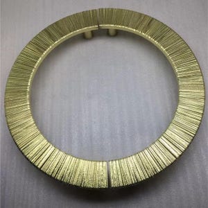May include: A gold-colored, circular decorative object with a textured, brush-like surface. The ring is split into two sections and appears to be made of metal. The object is likely a decorative element for furniture or interior design.