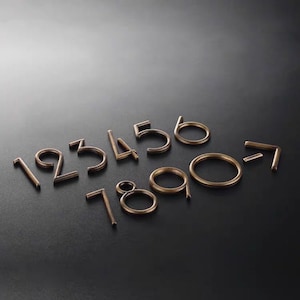 May include: A set of gold-toned metal numbers, 1 through 7, arranged in a semi-circle on a dark gray surface. The numbers are all in a simple, modern font.