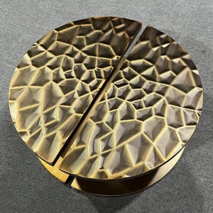 May include: A pair of bronze-colored, semi-circular cabinet pulls. Each pull has a textured, geometric pattern. The pulls are mounted on a matching base, suggesting a set for furniture or cabinetry. The design is modern and decorative.
