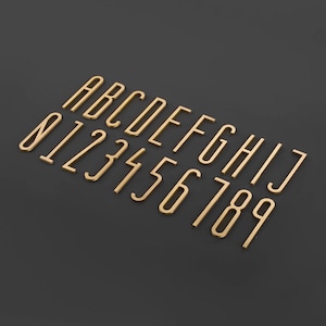 May include: Gold-colored metal alphabet and number characters on a black background. The letters are A through J and the numbers are 0 through 9.